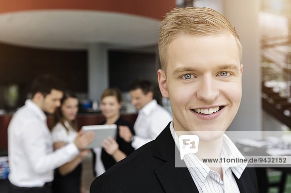 Lächelnder Geschäftsmann  Kollegen im Hintergrund mit digitalem Tablett