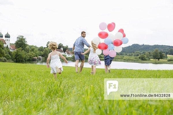 Familie läuft mit Luftballons durchs Feld