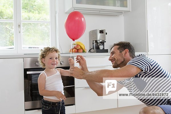 Mädchen hält Ballon mit Vater in der Küche