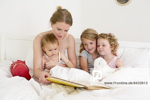 Mutter liest Buch zu drei Töchtern im Bett