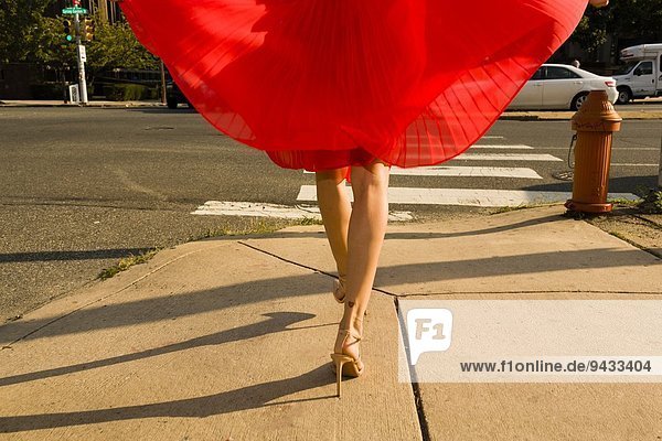 Taille unten Aufnahme einer jungen Frau  die den Bürgersteig entlang schlendert und einen roten Rock trägt.