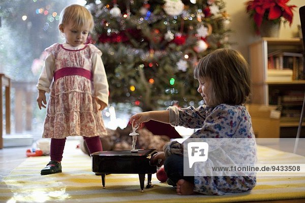 Zwei junge Schwestern  die zu Weihnachten eine Spieluhr mit Spielzeugklavier hören