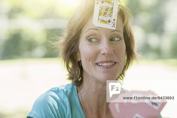 Reife Frau spielt Karten  eine Spielkarte auf die Stirn geklebt