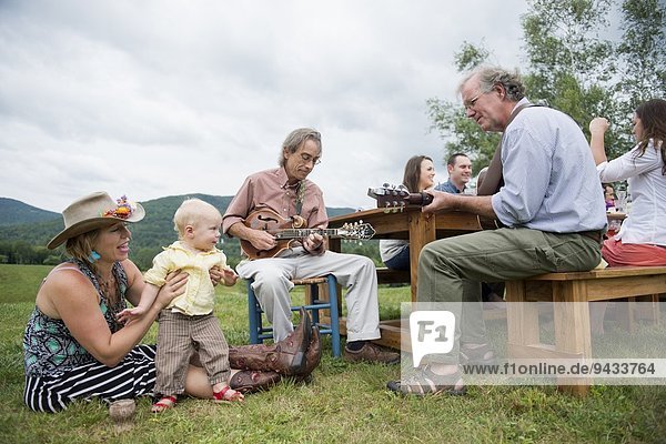 Zwei reife Familienmitglieder  die beim Familienessen im Freien musizieren.