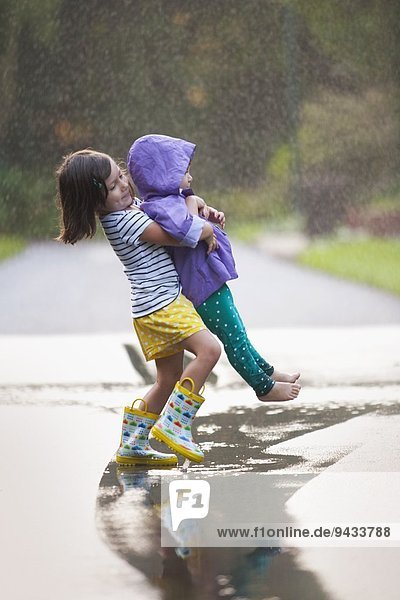 Mädchen trägt Kleinkind Schwester durch Pfütze auf der Straße