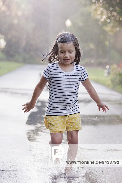 Barfuß-Mädchen läuft durch Pfützen auf regnerischer Straße