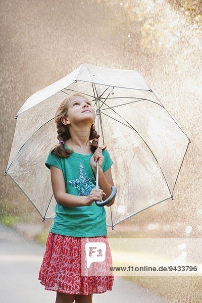 Mädchen hält Regenschirm auf regnerischer Straße hoch