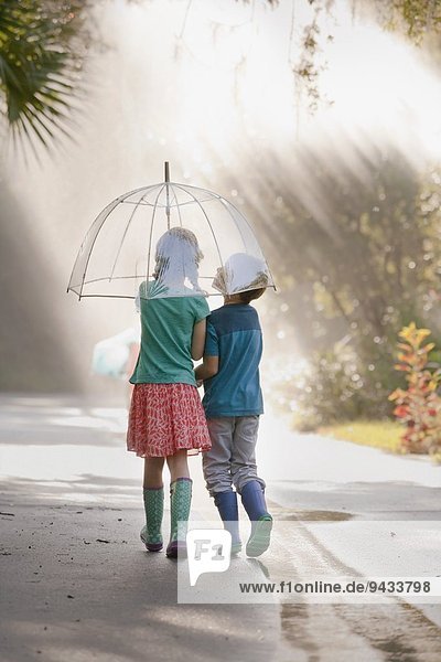 Rückansicht des Jungen und Mädchens mit Regenschirm auf der Straße