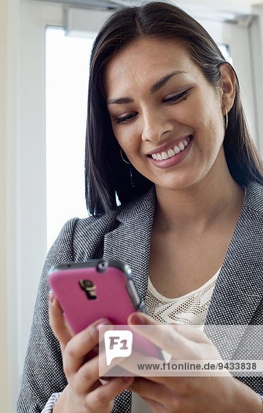 Junge Geschäftsfrau beim Betrachten von Texten auf dem Smartphone im Büro