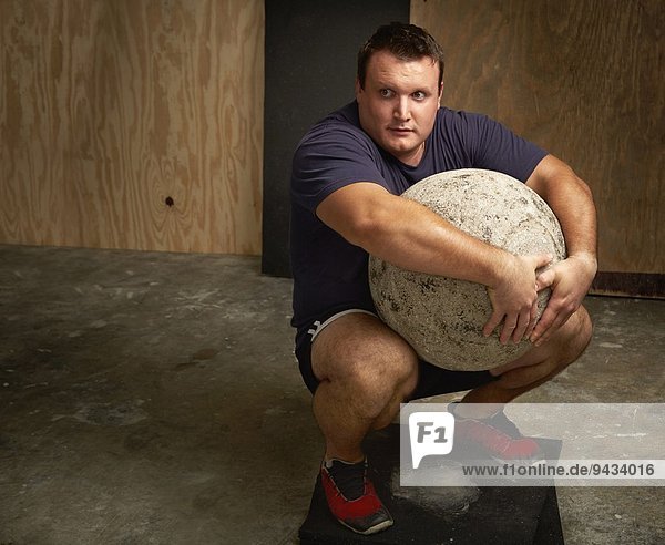 Portrait eines jungen  männlichen Gewichthebers mit Atlasball in der Turnhalle