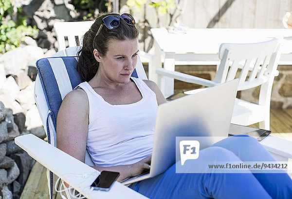 Mittlere erwachsene Frau mit Laptop auf dem Sessel im Hof