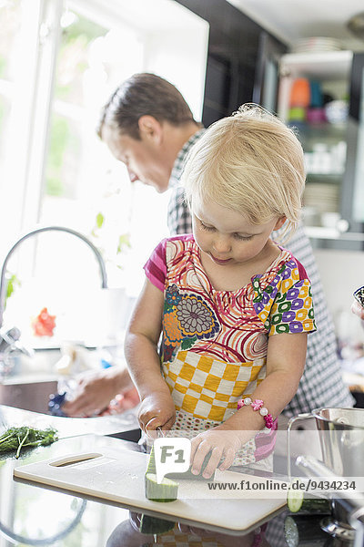 Mädchen hackt Gemüse  während der Vater das Geschirr im Hintergrund in der Küche putzt.