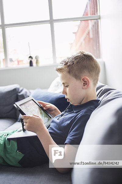 Seitenansicht des Jungen mit digitalem Tablett auf dem Sofa zu Hause