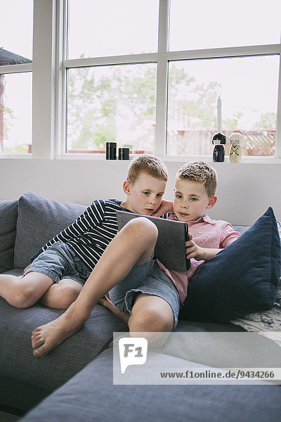 Siblings using digital tablet on sofa at home