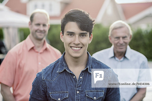 Porträt eines selbstbewussten jungen Mannes mit Großvater und Vater im Hof stehend