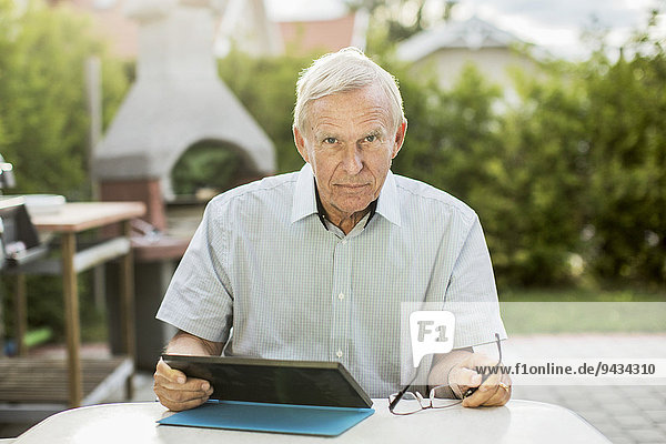 Portrait of confident senior man using digital tablet at table in yard