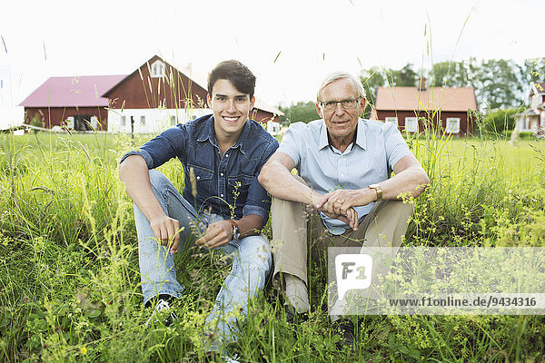 Full length portrait of grandfather and grandson sitting on grassy field