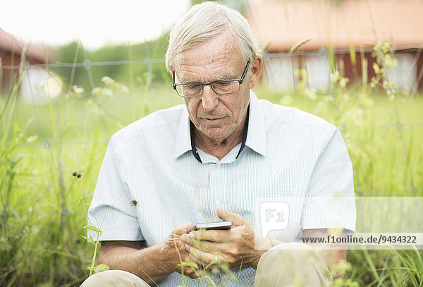 Senior Mann SMS auf dem Handy  während er im Hof sitzt.