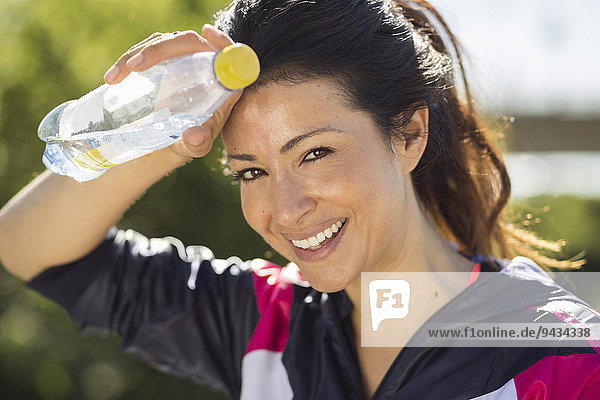 Porträt einer fröhlichen Frau  die den Schweiß wischt  während sie die Wasserflasche in der Hand hält.