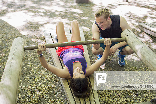 Mann ermutigt Frau beim Heben von Holzgewicht im Fitnessstudio im Freien