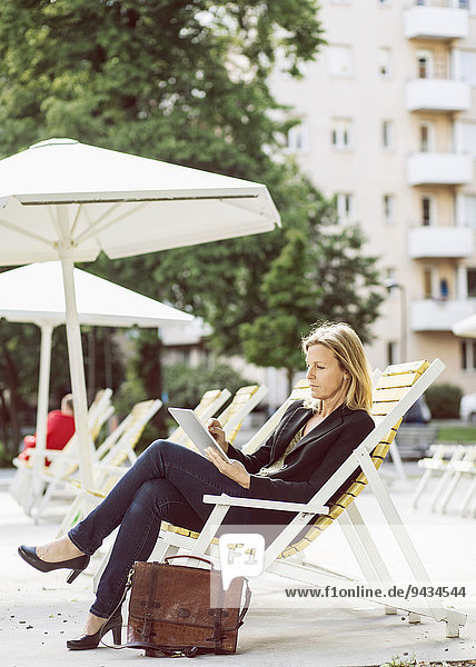 Volle Länge der Geschäftsfrau mit digitalem Tablett auf Sessel im Park