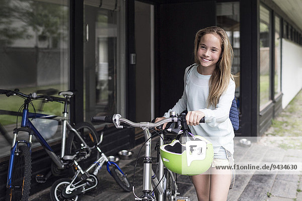 Fröhliches Mädchen beim Spaziergang mit dem Fahrrad vor dem Haus