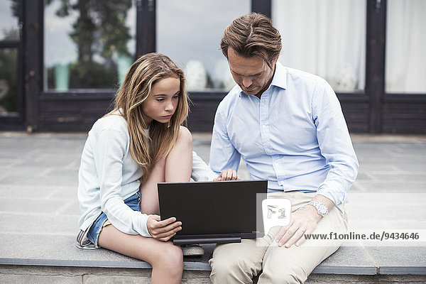 Vater und Tochter benutzen gemeinsam den Laptop auf der Veranda.
