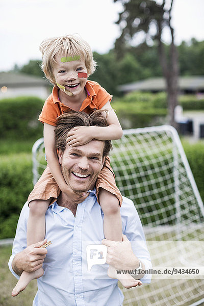 Portrait of happy father carrying injured boy on shoulders