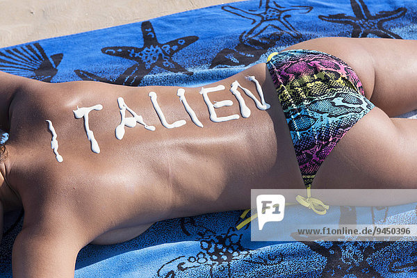 'Frau liegt am Strand  Schriftzug ''Italien'' aus Sonnencreme auf dem Rücken  Adria  Italien  Europa'
