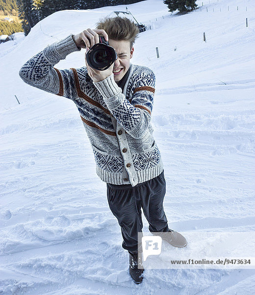Young man in the snow taking a picture with a digital SLR camera  Hochbrixen  Brixen im Thale  Tyrol  Austria  Europe