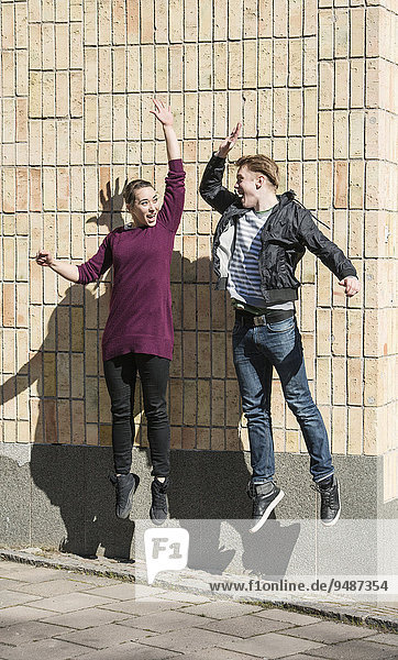 Ein junger Mann und eine Frau springen in die Luft und klatschen sich dabei ab  Schweden  Europa
