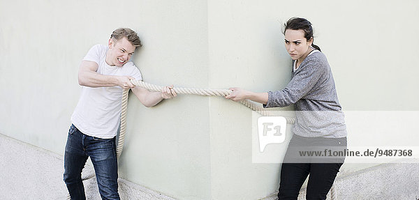 Ein wütendes Paar beim Tauziehen  das Tau liegt um die Ecke eines Hauses  Symbolbild  Konflikte in einer Beziehung  Gegner  Entschlusskraft