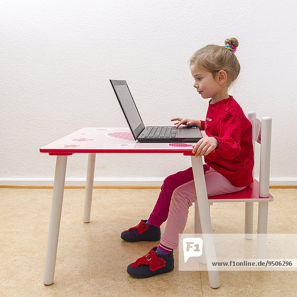 Girl  3 years  sitting at a table  using a laptop