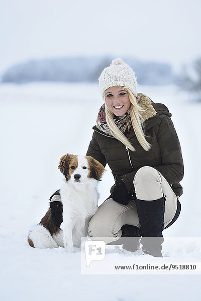 Junge Frau mit einem Kooikerhondje-Hund im Schnee