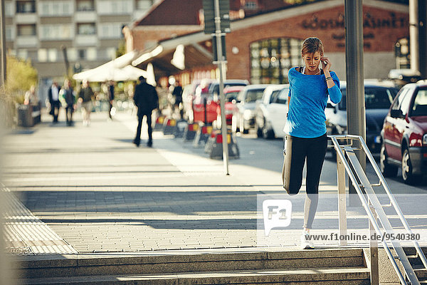 Young jogger stretching while on the phone