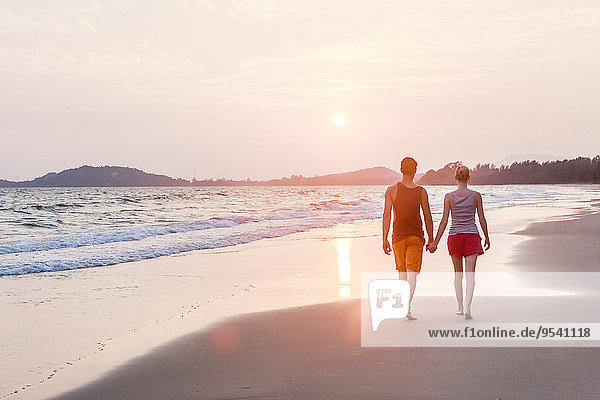 Young couple walking along beach at dusk