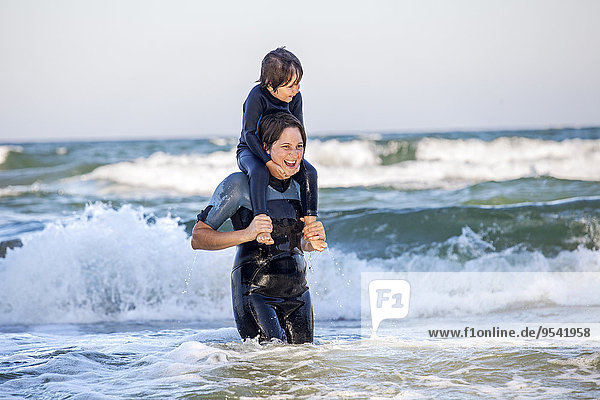 Mother carrying son on shoulders in sea