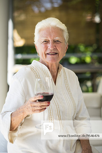 Porträt einer lächelnden Seniorin mit einem Glas Rotwein