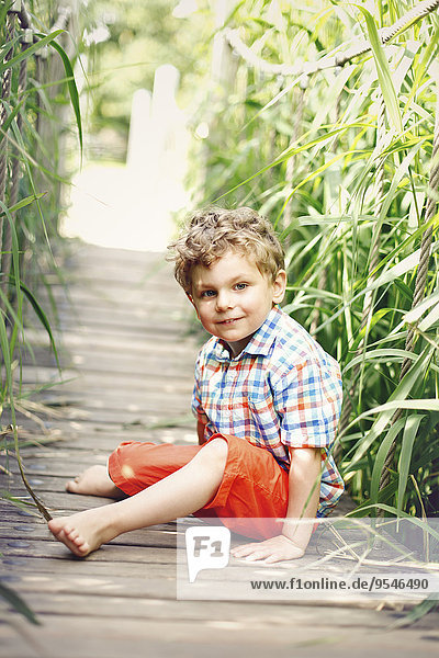Porträt eines kleinen Jungen  der auf einem Gehweg sitzt.