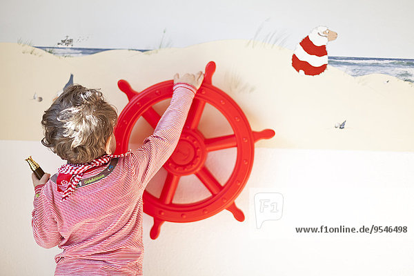 Kleinkind spielt mit rotem Rad an der Wand befestigt