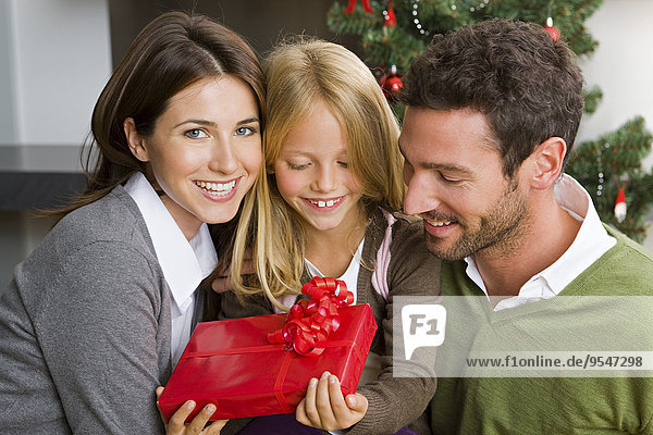 Glückliches Paar und ihre Tochter mit Weihnachtsgeschenk zu Hause