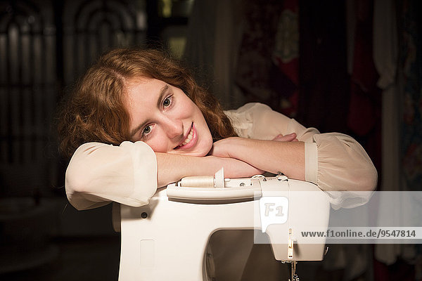 Porträt einer Modedesignerin  die sich in ihrem Atelier an die Nähmaschine lehnt.