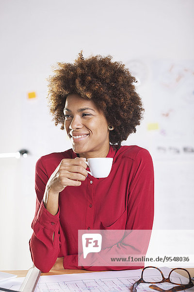 Porträt einer lächelnden jungen Architektin beim Kaffeetrinken am Schreibtisch