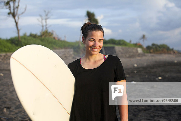 Indonesien  Bali  Canggu  Portrait der glücklichen jungen Frau mit Surfbrett am Strand