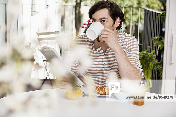 Mann mit Kaffee und Zeitung beim Frühstücken