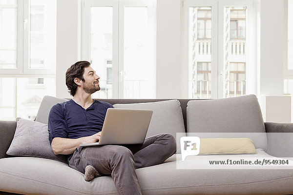 Mann auf der Couch sitzend mit Laptop