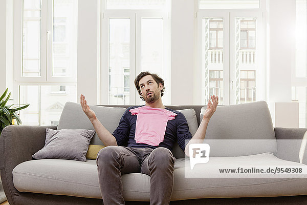 Enttäuschter Mann mit rosa Babyhemd auf der Couch