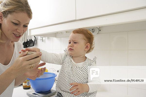 Mutter und kleine Tochter mit Smartphone in der Küche