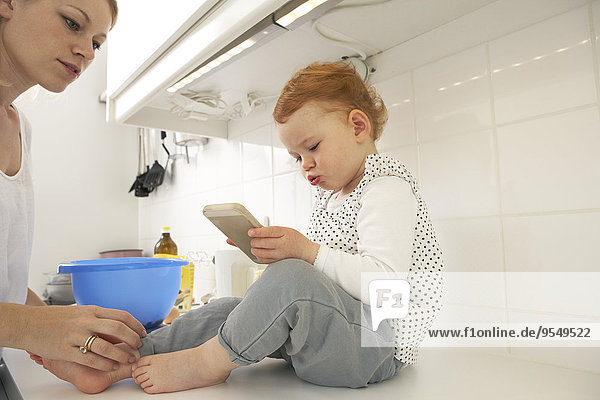 Little girl sitting on kitchen counter with smartphone
