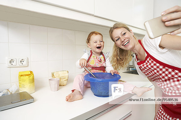 Young woman taking a selfie with her little daughter in their kitchen